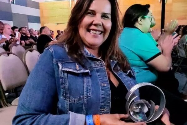 Diretora da Uniontec de jaqueta jeans sentada e segurando troféu de premiação no evento Senior Summit 2024